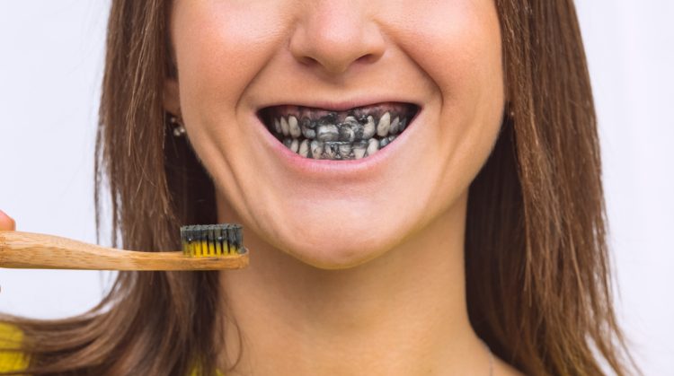 Woman brushing teeth with charcoal toothpaste, showing black-stained smile.